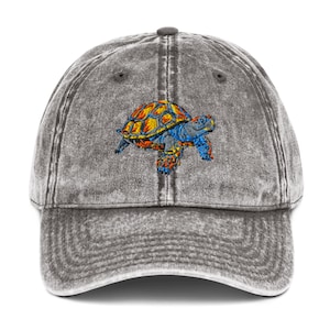May include: A gray baseball cap with a distressed finish. The cap features an embroidered turtle design in shades of blue, orange, and yellow. The turtle is centered on the front of the cap, offering a casual and stylish accessory.