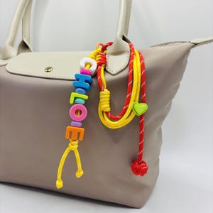 Porte-nom personnalisé pour breloques pour sac avec pompon, lettres acryliques de couleur aléatoire pour sac de plage, sac à dos, breloques de sac avec nom d'enfant, porte-nom personnalisé.