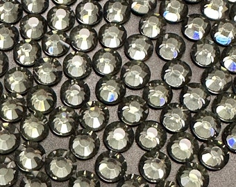 May include: A close-up of a large quantity of dark gray rhinestones arranged in a pattern. The rhinestones are faceted and have a slight iridescent sheen.