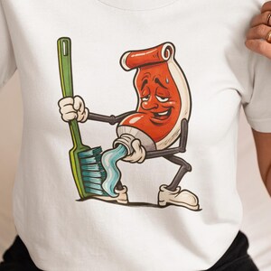 May include: White t-shirt featuring a cartoon illustration of a red and white tube of toothpaste with arms and legs, squeezing out blue toothpaste onto a green toothbrush. The cartoon character has a distressed expression.