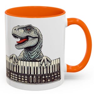 May include: White ceramic mug with an orange interior and handle. The mug features a detailed illustration of a dinosaur with its mouth open, appearing to play a synthesizer keyboard. The design is set against a white background.