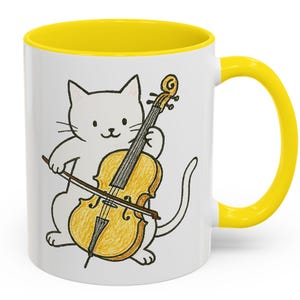 May include: White ceramic mug with a yellow rim and handle. The mug features a cartoon illustration of a white cat playing a cello.