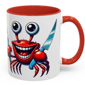 May include: White ceramic mug with a red interior and handle. The mug features a cartoon crab illustration with large eyes, a wide grin, and holding a knife. The crab is red with blue accents.