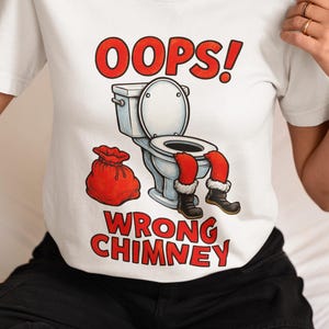 May include: White t-shirt with a humorous Christmas graphic. The design features the text "OOPS! WRONG CHIMNEY" in red, along with an illustration of Santa's legs stuck in a toilet and a red gift bag.