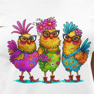 May include: White t-shirt featuring a colorful illustration of three anthropomorphic chickens wearing glasses and floral accessories. The chickens are adorned in vibrant outfits with floral and patterned designs. The artwork has a whimsical and playful style.