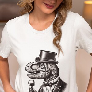 May include: White t-shirt featuring a detailed illustration of a dinosaur in a tuxedo, top hat, and monocle, holding a glass of wine. The design is in black and white, creating a sophisticated and humorous aesthetic.