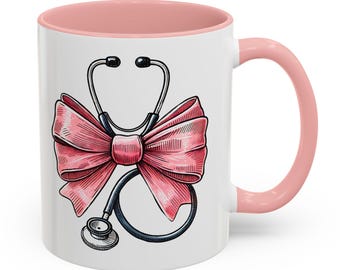 May include: White ceramic coffee mug with a pink rim and handle. The mug features a pink bow with a stethoscope in the center.