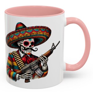 May include: White ceramic coffee mug with a pink rim. The mug features a colorful illustration of a skeleton wearing a sombrero and holding a rifle.
