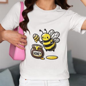 May include: White t-shirt featuring a cartoon bee holding a honey dipper next to a honey pot. The bee is yellow and black with a smiling face. The honey pot is brown with the word "HONEY" on it.