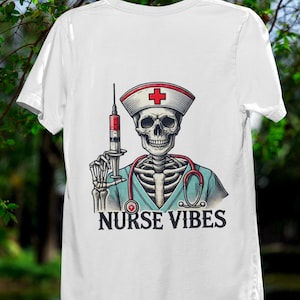 May include: White t-shirt featuring a skeleton in a nurse's uniform, holding a syringe. The skeleton wears a nurse's cap with a red cross and a stethoscope. The text "NURSE VIBES" is printed below the skeleton.