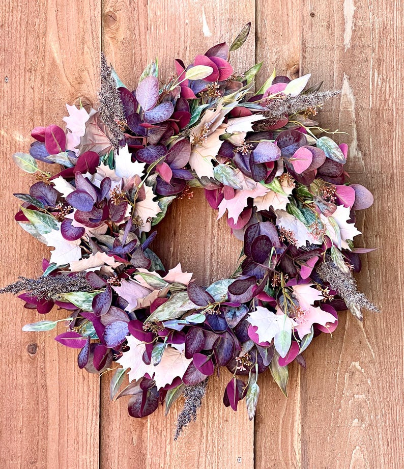 May include: A purple and white fall wreath with eucalyptus leaves, maple leaves, and dried flowers.