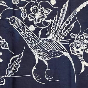 May include: A dark blue textile featuring a white, detailed illustration of a bird with long tail feathers, surrounded by floral and leaf motifs. The design has a batik-like appearance, with intricate patterns and a handcrafted aesthetic.