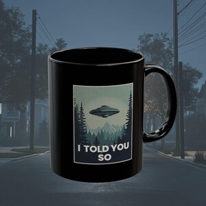 May include: Black coffee mug with a graphic of a flying saucer and the text "I told you so".