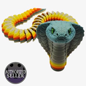 May include: A 3D-printed cobra snake toy in shades of blue, grey, yellow, orange, and red. The snake's head is a light blue-grey with green eyes. The body is segmented, allowing for flexible movement. The image includes an "AUTHORIZED SELLER" logo.
