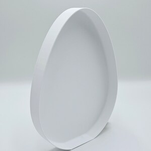 May include: White ceramic egg-shaped tray with a smooth, rounded surface and a slightly raised rim.