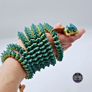 May include: A green and orange segmented dragon toy with a spiky texture. The toy is coiled around a person's wrist.
