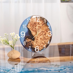 May include: A blue and brown resin clock with white numbers and a gold-colored hand. The clock is on a clear stand and has a wood grain pattern.