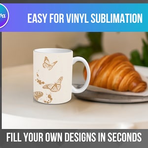 May include: White ceramic mug with a design of gold butterflies on a white background. The mug is sitting on a white surface with a croissant in the background.
