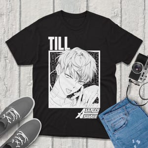 May include: Black t-shirt featuring a black and white anime-style illustration of a person with the word "TILL" above the image. The text "TEEN STAGE" is below the illustration. Gray sneakers and blue jeans are visible.