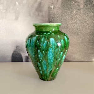 Peut inclure: Un petit vase en céramique vert brillant. Le vase a un corps arrondi et un col étroit. L'émail présente un mélange de teintes vertes et turquoise, créant un effet dégoulinant. Le vase est un objet décoratif.