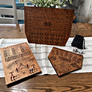 Könnte beinhalten: Drei Spielbretter aus Holz mit eingravierten Details. Ein großes rechteckiges Brett mit der Aufschrift Michigan, ein rechteckiges Texas Rangers Baseball-Brett mit Stiften und ein Brett in Form einer Home Plate mit der Aufschrift Ava. Enthält zwei weiße Würfel und einen schwarzen Beutel.