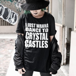 May include: A black t-shirt with white text that reads "I just wanna dance to crystal castles". The person wearing the shirt is wearing a black hat and black pants.