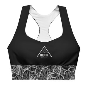 May include: Black sports bra with a white inner lining and a white logo that says "Monk zenwear" in a triangle. The bottom of the bra has a white and black patterned design.