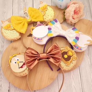 May include: A selection of character-themed headbands. One features a large yellow bow and gold sequined ears. Another has a white sequined bow with colourful accents. A third headband has a brown bow. The headbands are on a wooden surface.