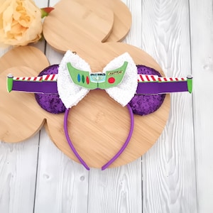 May include: A purple headband with sequined ears and a white bow featuring a green and white design with the text "SPACE RANGERS LIGHTYEAR". The headband has a purple band and a green and purple striped design.