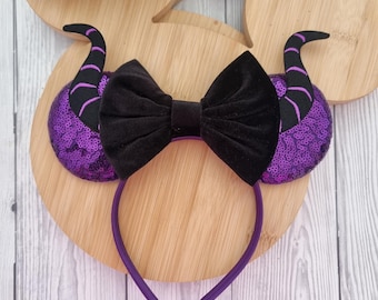 Op de afbeelding: Een paarse hoofdband met pailletten, zwarte hoorns en een zwarte fluwelen strik. De hoofdband is paars en de hoorns hebben zwart-paarse strepen. De strik is gecentreerd op de hoofdband.