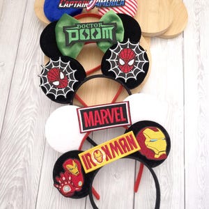 Pode incluir: Uma coleção de tiaras temáticas com personagens da Marvel. Os designs incluem Capitão América, Doutor Destino, Homem-Aranha e Homem de Ferro. Cada tiara tem um design único com logotipos e cores de personagens, em orelhas pretas ou brancas.