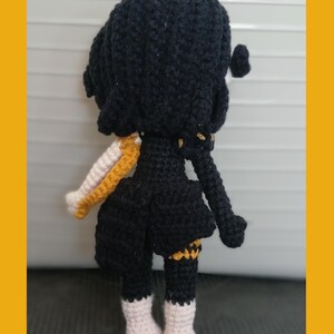 May include: Crocheted doll with black hair and a black dress. The doll has white and gold accents on the sleeves and legs. The doll is wearing white boots. The doll is handmade.