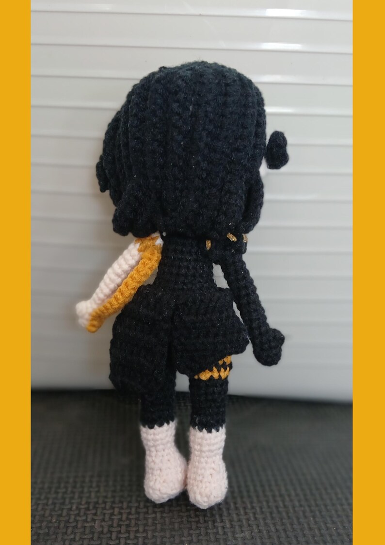 May include: Crocheted doll with black hair and a black dress. The doll has white and gold accents on the sleeves and legs. The doll is wearing white boots. The doll is handmade.