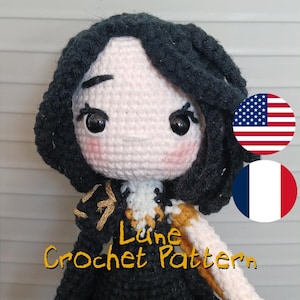 May include: A handmade crochet doll with a black dress and hair, and a light skin tone. The doll has rosy cheeks and large black eyes. The text "Lune Crochet Pattern" is written in yellow cursive. The American and French flags are in the background.