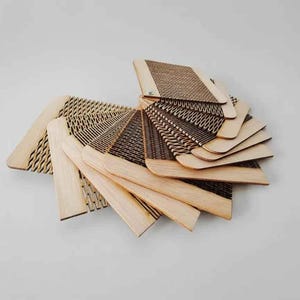 Puede incluir: Una colecci&oacute;n de muestras de madera cortadas con l&aacute;ser, dispuestas en abanico para mostrar varios patrones. Las muestras, de color marr&oacute;n claro, presentan dise&ntilde;os intrincados, incluyendo texturas geom&eacute;tricas y tejidas. La disposici&oacute;n se encuentra sobre un fondo blanco liso.
