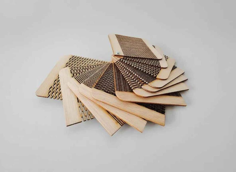 Puede incluir: Una colecci&oacute;n de muestras de madera cortadas con l&aacute;ser, dispuestas en abanico para mostrar varios patrones. Las muestras, de color marr&oacute;n claro, presentan dise&ntilde;os intrincados, incluyendo texturas geom&eacute;tricas y tejidas. La disposici&oacute;n se encuentra sobre un fondo blanco liso.