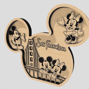 May include: Wooden Mickey Mouse head-shaped wall art featuring Mickey and Minnie Mouse, and the Golden Gate Bridge. The words "San Francisco" are in the center. The art is made of light-colored wood with black outlines.