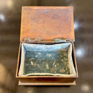 May include: An open antique copper box with a green velvet lining. The box has a worn, aged patina and is made of solid metal.
