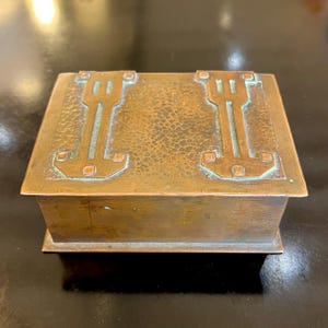 May include: A rectangular copper box with a hammered finish and geometric designs on the top. The box has a slightly raised edge around the top and a smooth bottom.