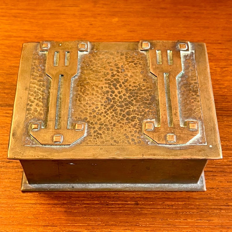 May include: A rectangular copper box with a hammered finish and geometric designs. The box has a hinged lid and a raised edge.
