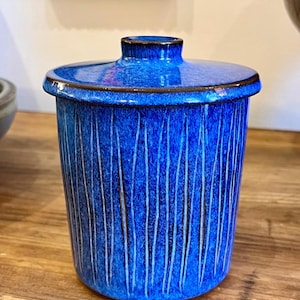 May include: A blue ceramic jar with a lid, featuring a vertical striped pattern. The jar has a glossy finish and a dark blue rim.