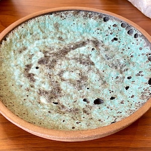 Puede incluir: Un cuenco redondo de cerámica hecho a mano con un interior texturizado turquesa y marrón. El cuenco tiene un borde marrón claro y un diseño único. El cuenco es adecuado para servir alimentos o como pieza decorativa. Diámetro: aprox. 20 cm.