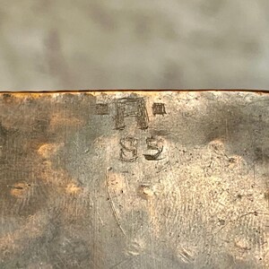 May include: Close-up of a metal surface with the inscription "A" and "85" etched into it.