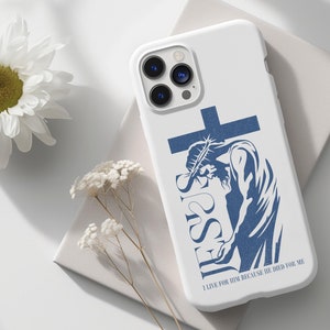 May include: White iPhone case featuring a blue silhouette of Jesus on the cross. The text "JESUS" is written vertically on the left side of the image. The text "I LIVE FOR HIM BECAUSE HE DIED FOR ME" is written below the image.