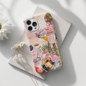 Op de afbeelding: Een roze en witte iPhone-hoes met een collage van afbeeldingen, waaronder een kopje koffie, een croissant, een ballon en een gebouw. De tekst "What a Sweet Heaven" is zichtbaar op de hoes.