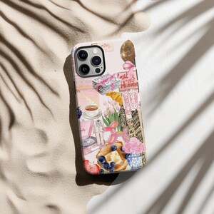 Op de afbeelding: Een roze en witte iPhone-hoes met een collage van afbeeldingen, waaronder een croissant, bloemen, een kopje koffie, een platenspeler en een gebouw. De tekst "What a mess! Heaven" is zichtbaar op de hoes.