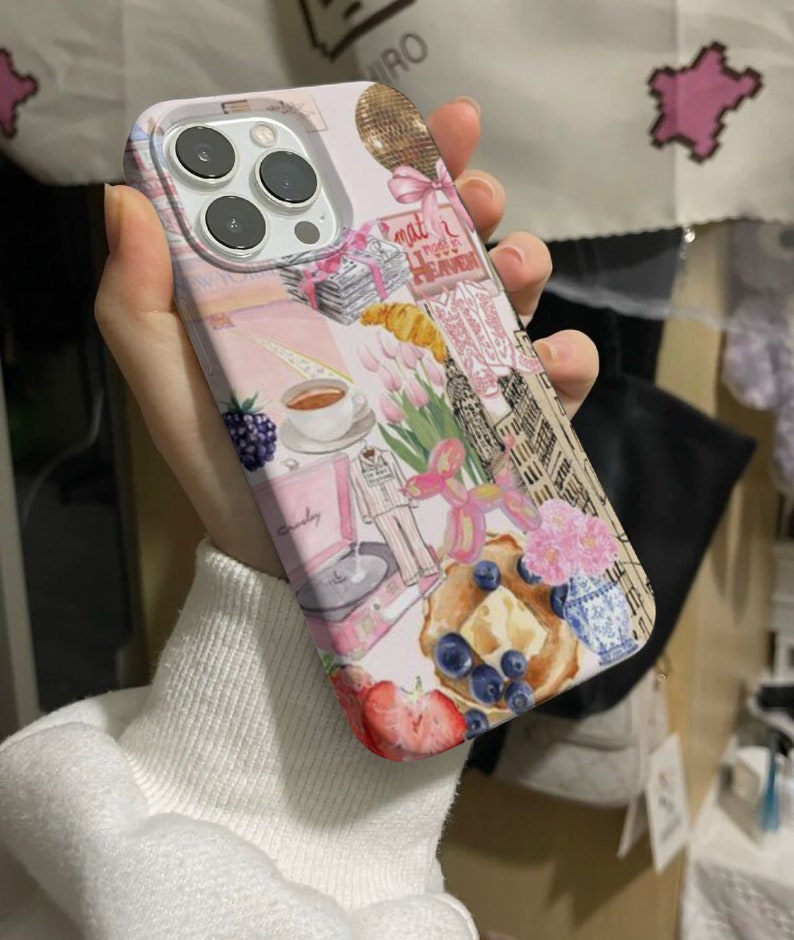 Op de afbeelding: Een roze en witte iPhone-hoes met een collage van afbeeldingen, waaronder een discobal, een kopje koffie, een platenspeler, een croissant en een bos tulpen. De tekst "what I need is a vacation" is zichtbaar op de hoes.