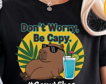 May include: Black t-shirt with a cartoon capybara wearing sunglasses, a cocktail, and the text "Don't Worry, Be Capy." The shirt also includes the hashtag "#CapyVibes."