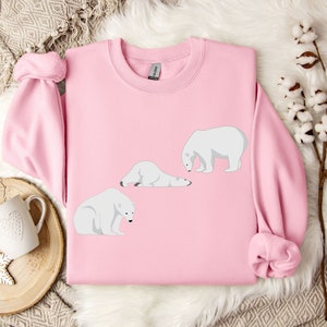 Peut inclure: Un sweat-shirt rose avec un motif de trois ours polaires blancs dans diff&eacute;rentes poses. Les ours sont tous tourn&eacute;s vers la gauche de l'image.