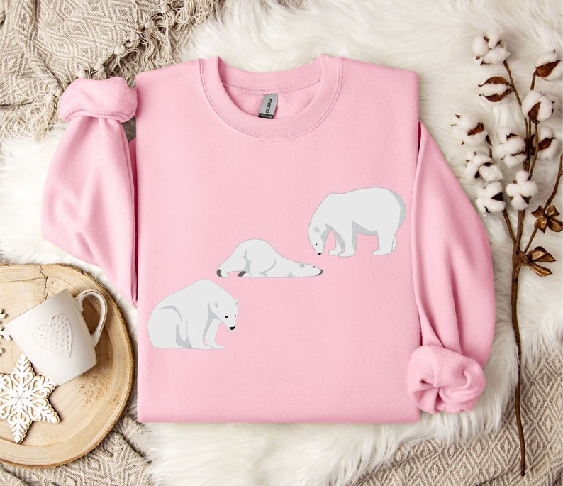 Peut inclure: Un sweat-shirt rose avec un motif de trois ours polaires blancs dans diff&eacute;rentes poses. Les ours sont tous tourn&eacute;s vers la gauche de l'image.